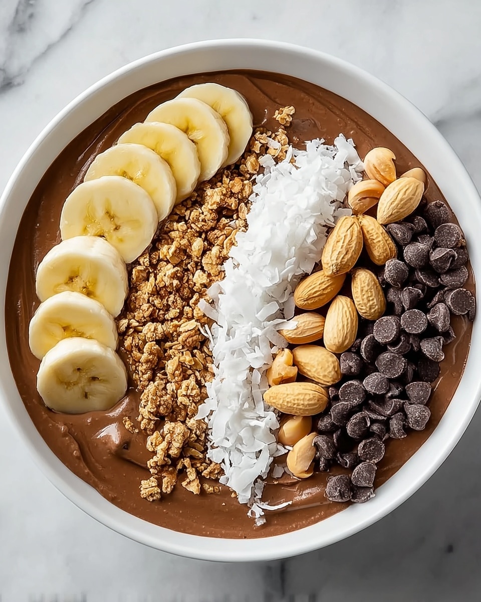 A round white bowl filled with a smooth light brown smoothie base swirled in the center with a thick peanut butter layer. On top, there are evenly arranged layers of banana slices on the left, golden granola next to it, white coconut flakes, and dark chocolate chips on the right side. The bowl is placed on a white marbled board with a small amount of chopped peanuts and chocolate chips scattered around it. Four small white bowls surround the main bowl, each containing peanut butter, cocoa powder, chopped nuts, and chocolate chips. Photo taken with an iphone --ar 4:5 --v 7